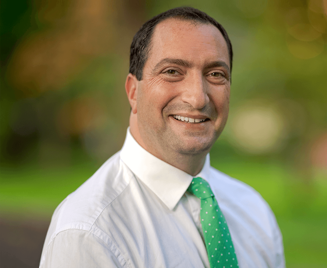 Scott Goldberg, middle aged white male with dark brown hair wearing white shirt with a green tie.